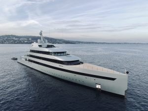 A long white superyacht standing on dark blue waters on a clear day.