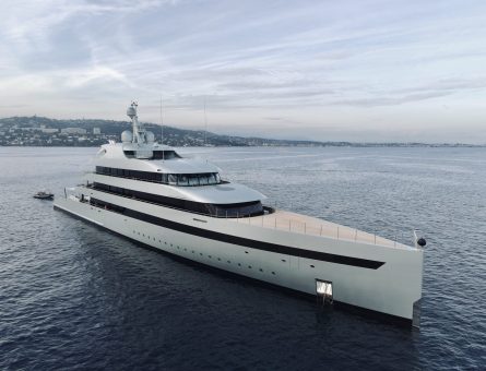 A long white superyacht standing on dark blue waters on a clear day.