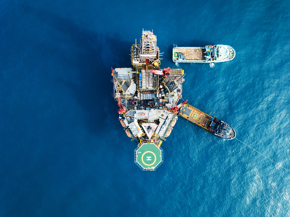 Birdseye view of offshore platform with helipad and two vessels sailing away